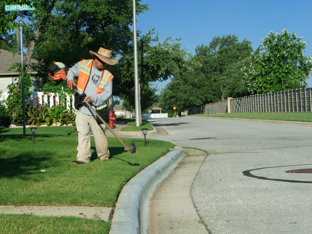 Lawn maintenance crew member string trimming the lawn edge along a curb
